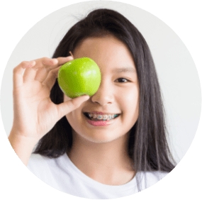 Young girl holding up an apple smiling and wearing braces